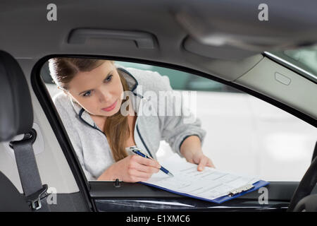 Femmina tecnico di manutenzione con appunti esame auto di interni in officina Foto Stock