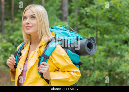 Donna sorridente backpacker in impermeabile che guarda lontano a forest Foto Stock