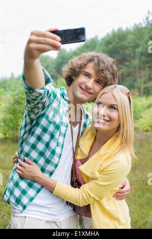 Felice coppia giovane tenendo ritratto di auto attraverso il telefono cellulare nel campo Foto Stock