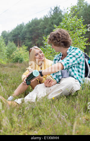 Escursionista maschio versando il caffè per donna mentre vi rilassate nel campo Foto Stock