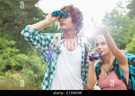 Escursionista maschio utilizzando un binocolo mentre la donna che mostra lui qualcosa in foresta Foto Stock