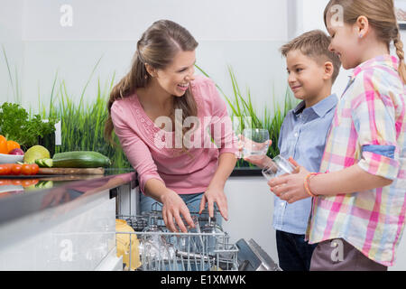 Felice madre e bambini ponendo i bicchieri in lavastoviglie Foto Stock