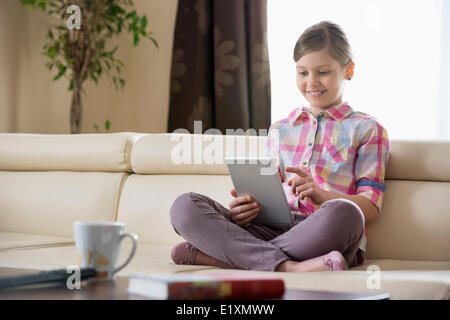 Sorridente ragazza utilizzando digitale compressa sul divano di casa Foto Stock