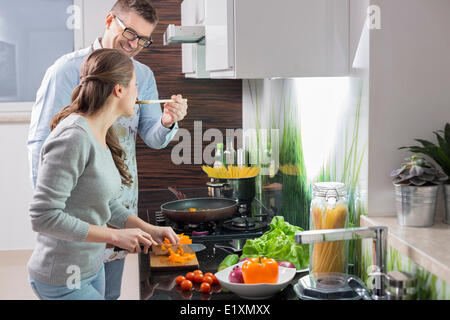 Uomo felice di alimentazione per alimentare la donna come tagliare le verdure in cucina Foto Stock