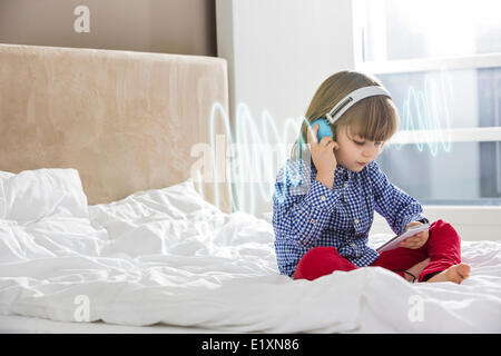 Lunghezza completa di boy ascoltando la musica attraverso le cuffie sul letto Foto Stock