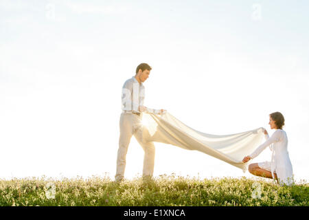 Vista laterale della donna e uomo diffondere Coperta picnic sull'erba durante la giornata di sole Foto Stock