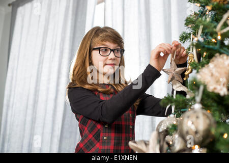 Ragazza adolescente hanging ornamento su albero di Natale a casa Foto Stock