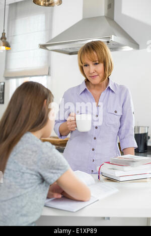 Azienda madre tazza di caffè mentre guardano la ragazza che studiano in cucina Foto Stock