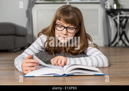 Ragazza adolescente lettura libro mentre giacente sul piano a casa Foto Stock