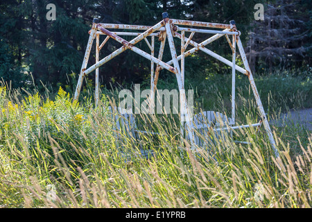 Un vecchio arrugginito lawn swing abbandonati in erba alta. Foto Stock