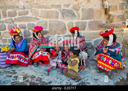 Donne e bambini in abito tradizionale degli Indiani Quechua seduta sul pavimento di fronte a un muro, Ollantaytambo Foto Stock