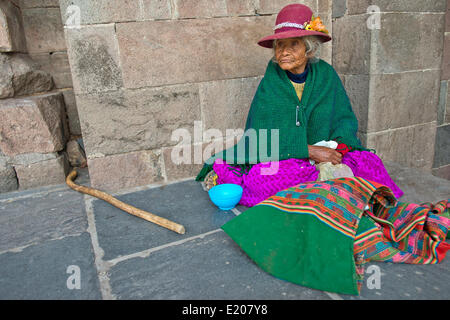 Una donna anziana in abito tradizionale degli Indiani Quechua seduta sul pavimento di fronte a un muro Inca, Provincia di Cusco, Perù Foto Stock