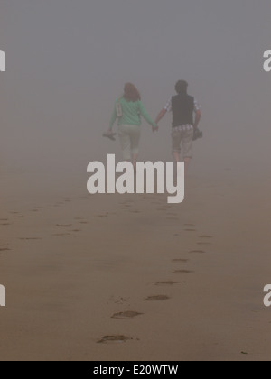 Coppia di mezza età camminando mano nella mano nella spessa nebbia di mare, Padstow, Cornwall, Regno Unito Foto Stock