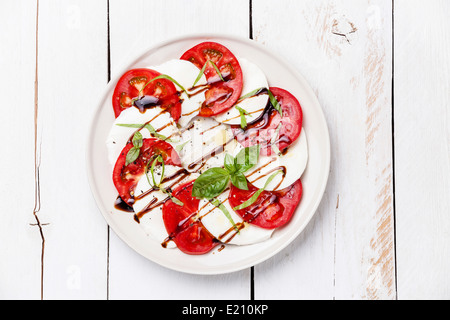 Insalata caprese con pomodoro e fettine di mozzarella con foglie di basilico bianco su sfondo di legno Foto Stock