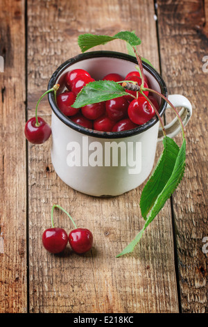 Vintage mug di ciliegie fresche con foglie sul vecchio tavolo in legno Foto Stock