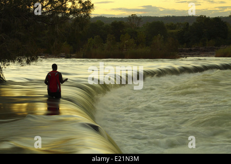 Un uomo solitario utilizza una linea a mano per la pesca al barramundi Ivanhoe attraversando il fiume Ord - Kununurra, Western Australia. Foto Stock