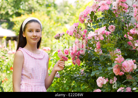 Ragazza adolescente nel paese giardino con rose di fioritura e boccola Foto Stock