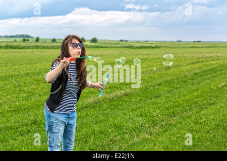 Bella giovane donna fare soffiare bolle, sull'erba verde Foto Stock