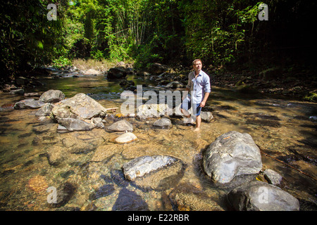 L'uomo ad esplorare una lussureggiante foresta pluviale sempreverde in streaming in Khao Sok National Park, Thailandia Foto Stock