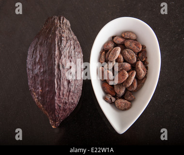 Le fave di cacao in una ciotola accanto al cacao Cialde da cui provengono. Foto Stock