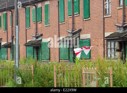 Un twisted San Giorgio bandiera si blocca sulla linea di lavaggio della sola casa occupata in via di intavolato case in Port Clarence vicino a Middlesbrough, England, Regno Unito Foto Stock