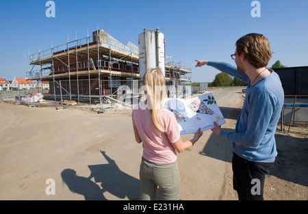 Coppia giovane con blueprint guardando come la loro casa è in fase di costruzione Foto Stock