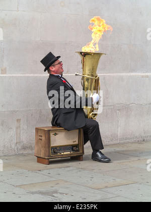 Busker, Christopher Werkowicz giocando la sua fiammante tuba seduto su una vecchia radio contro un semplice muro di pietra Londra Inghilterra Foto Stock