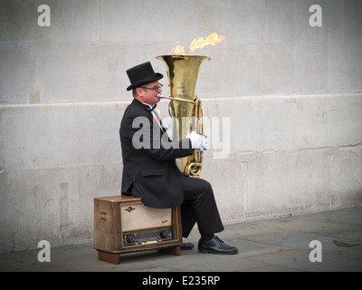 Busker, Christopher Werkowicz giocando la sua fiammante tuba seduto su una vecchia radio contro un semplice muro di pietra Londra Inghilterra Foto Stock