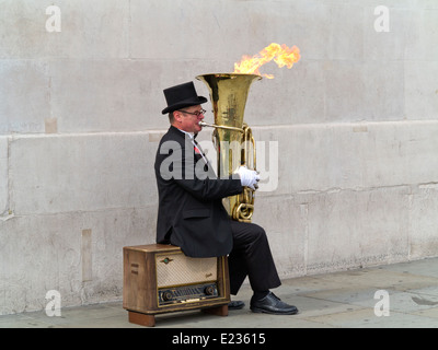 Busker, Christopher Werkowicz giocando la sua fiammante tuba seduto su una vecchia radio contro un semplice muro di pietra Londra Inghilterra Foto Stock