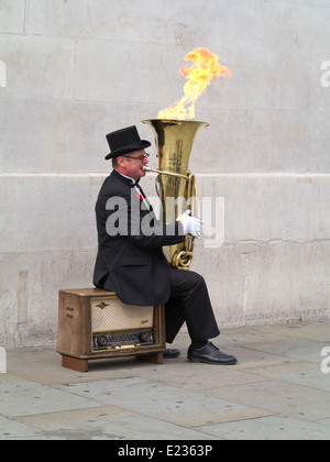 Busker, Christopher Werkowicz giocando la sua fiammante tuba seduto su una vecchia radio contro un semplice muro di pietra Londra Inghilterra Foto Stock