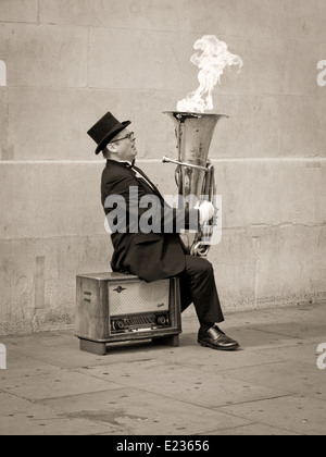 Busker, Christopher Werkowicz giocando flaming tuba seduto su una vecchia radio contro un semplice muro di pietra in seppia Foto Stock