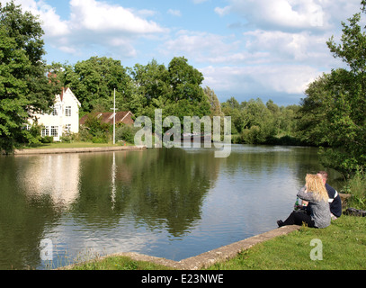 Giovane seduto sul greto del fiume gustando una birra in una serata estiva, Fiume Tamigi vicino a Oxford, Regno Unito Foto Stock