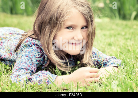 Adorabile ragazza distesa su erba guardando daisy Foto Stock