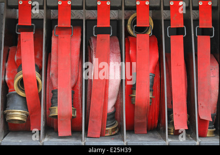 Sei tubi flessibili rosso dei vigili del fuoco in ordine all'interno del camion dei pompieri pronto a mettere fuori fuoco Foto Stock