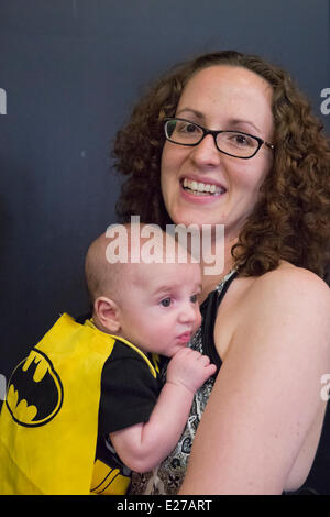 Città Giardino, New York, Stati Uniti - Giugno 14, 2014 - DANA MONTANO HARITOS sta tenendo il suo due-mese-vecchio figlio bambino vestito come BAT BABY, indossando un giallo e nero bat cape e tuta, a Biella eterna, annuale di Cultura Pop Expo che si terrà presso la Culla del Museo dell'aviazione sull'Isola Lunga. Credito: Ann e Parry/Alamy Live News Foto Stock