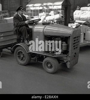 Degli anni Cinquanta, storici in uniforme Briitsh Ferrovie porter dell'atrio a Londra la stazione ferroviaria di Waterloo su un piccolo veicolo motorizzato il traino di un rimorchio spostamento di pacchetti. Foto Stock