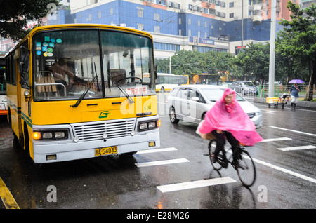 Un ciclista in un capo impermeabile passa su un vecchio autobus in un giorno di pioggia; escursioni in bicicletta in caso di maltempo Foto Stock