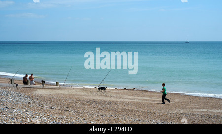Gli uomini la pesca sulla spiaggia a Worthing come una donna cammina il suo cane Foto Stock