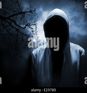 Uomo pericoloso che si nasconde sotto il cofano nella notte oscura foresta Foto Stock