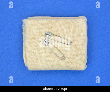 Un unico piegato pronto soccorso mussola bendaggio triangolare con due perni di sicurezza sulla cima di uno sfondo blu. Foto Stock