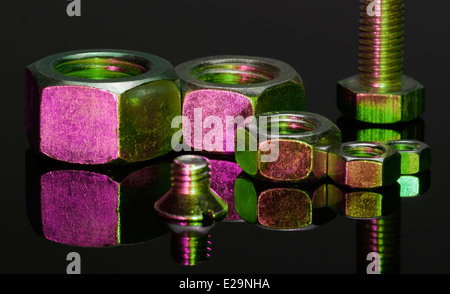 Alcuni viola e verde illuminato avvitare i dadi e una vite in nero riflettente sul retro Foto Stock