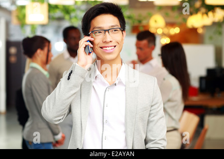 Ritratto di un imprenditore sorridente parlando sullo smartphone di fronte ai colleghi Foto Stock