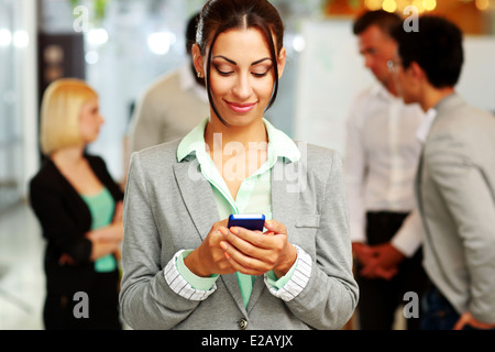 Ritratto di un felice imprenditrice utilizza lo smartphone di fronte ai colleghi Foto Stock