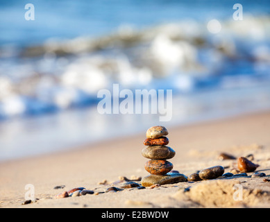 Piramide di pietre sulla sabbia che simboleggiano zen, armonia, equilibrio, blu oceano sullo sfondo . Foto Stock
