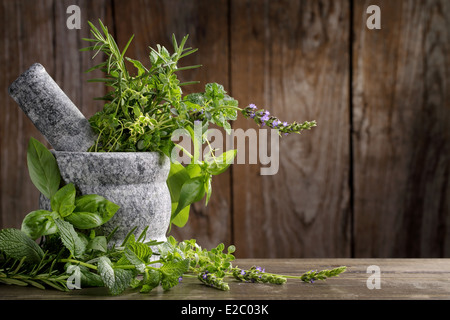 Le erbe in un mortaio su sfondo di legno Foto Stock