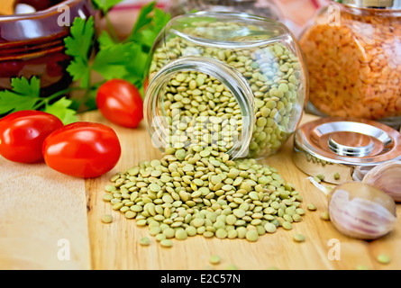 Le lenticchie verdi in un barattolo di vetro, prezzemolo, aglio, pomodori, pentola di creta, igienico sullo sfondo delle tavole di legno Foto Stock