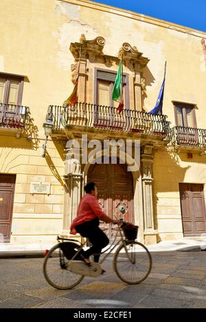 L'Italia, Sicilia, Trapani, centro storico, Fardella Fontana palace, donna su una bici passando davanti ad una porta di legno Foto Stock