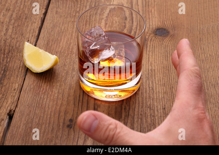 Il whiskey con cubetti di ghiaccio nel bicchiere e afferra la mano, close up Foto Stock