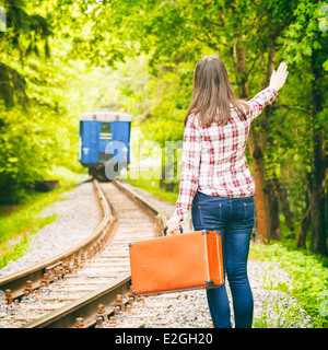 Giovane donna con la vecchia valigia agitando la mano, partenza treno sullo sfondo Foto Stock