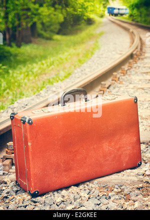 Vintage valigia marrone sulla ferrovia, treno blu è spento Foto Stock